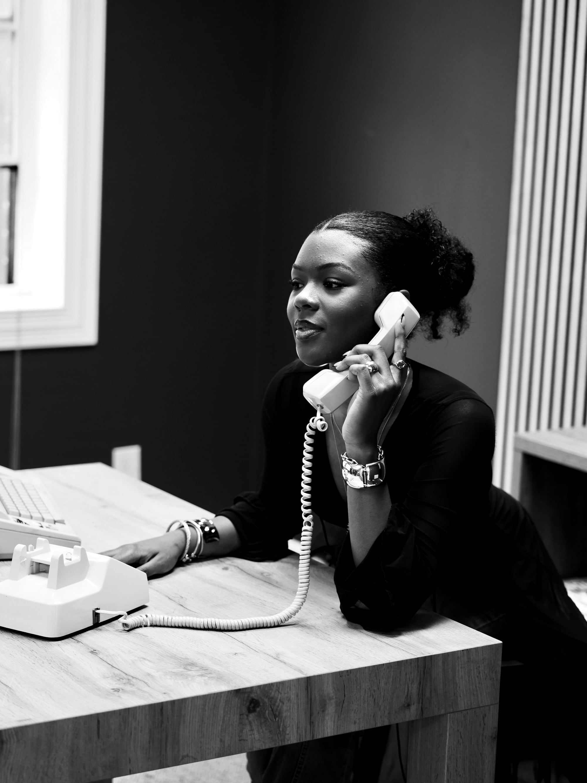 A woman mid-conversation on a corded desk telephone, photographed in black and white