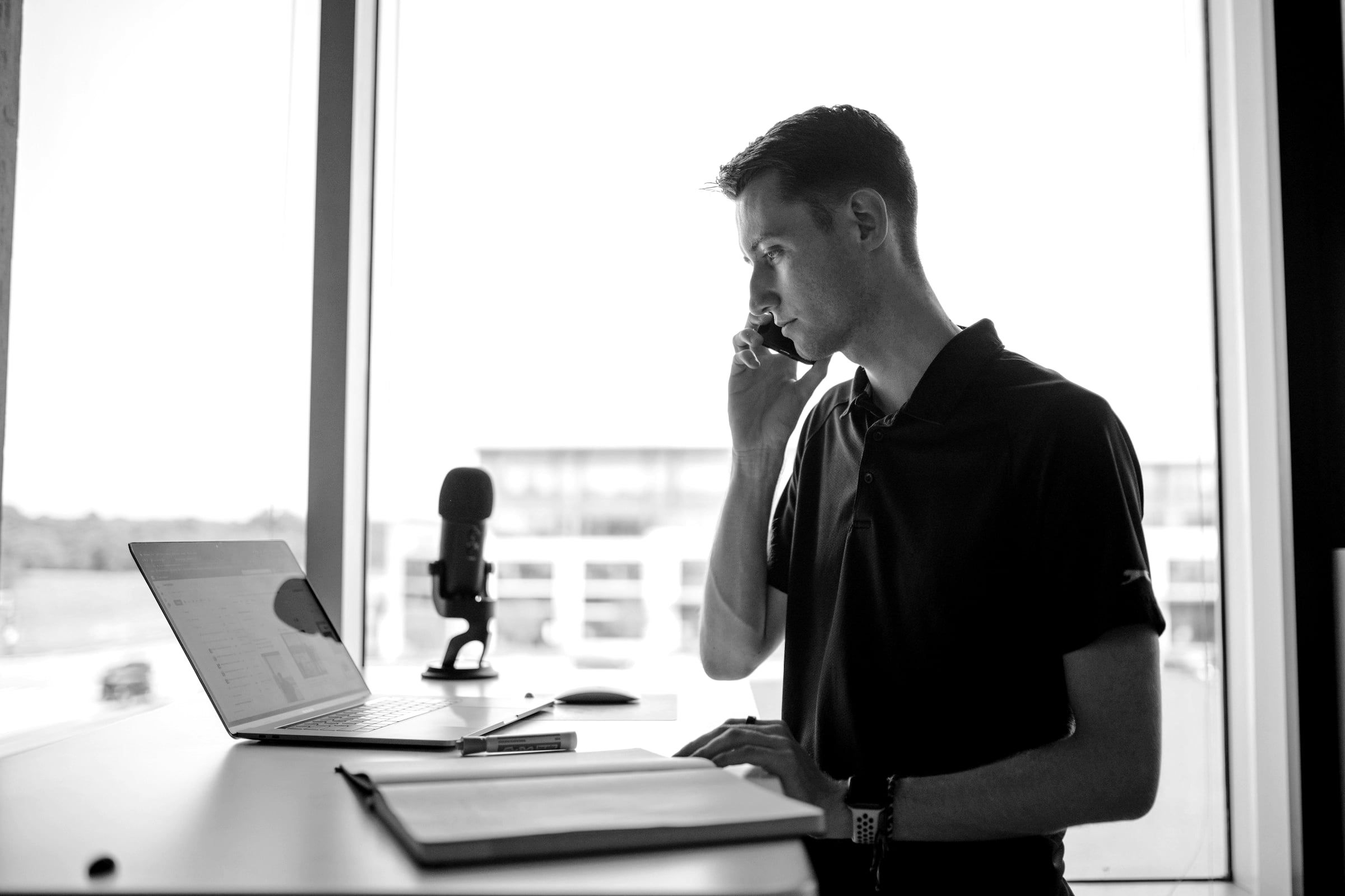 A man on a phone call at a standing desk by a window